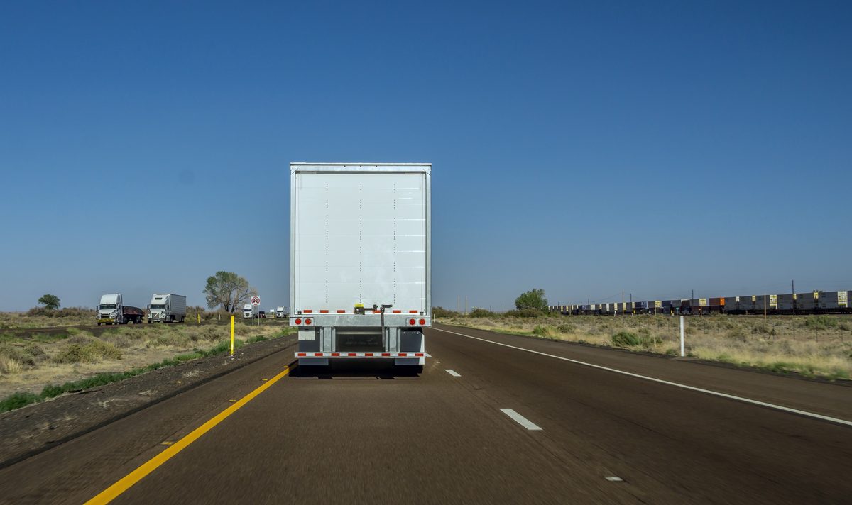 The back of a white trailer on a two-lane desert highway