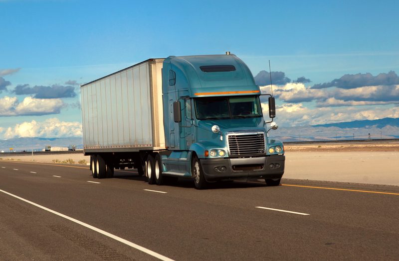 A teal semi truck with a white trailer on a desert highway